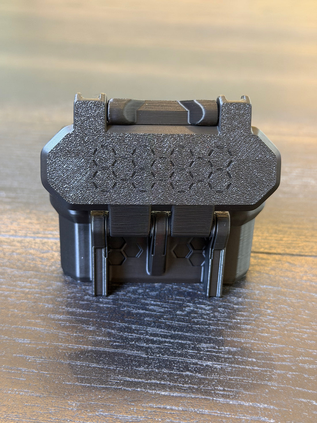 Closed black 3D-printed vial case shown from the back hinge side, resting on a dark wood surface.