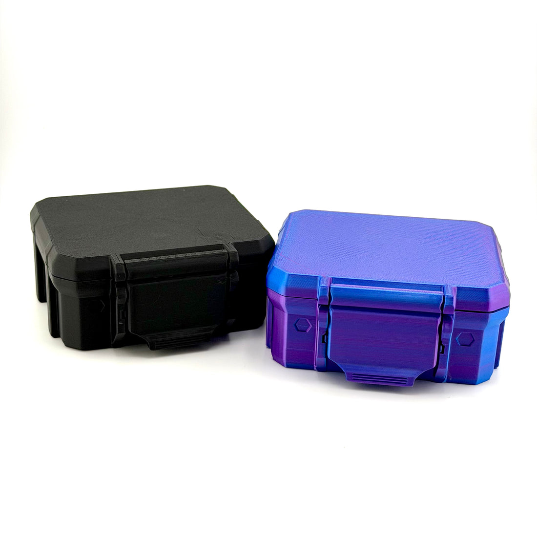 Two closed 3D-printed hard-shell vial cases in black and shimmering purple-blue with front latches.