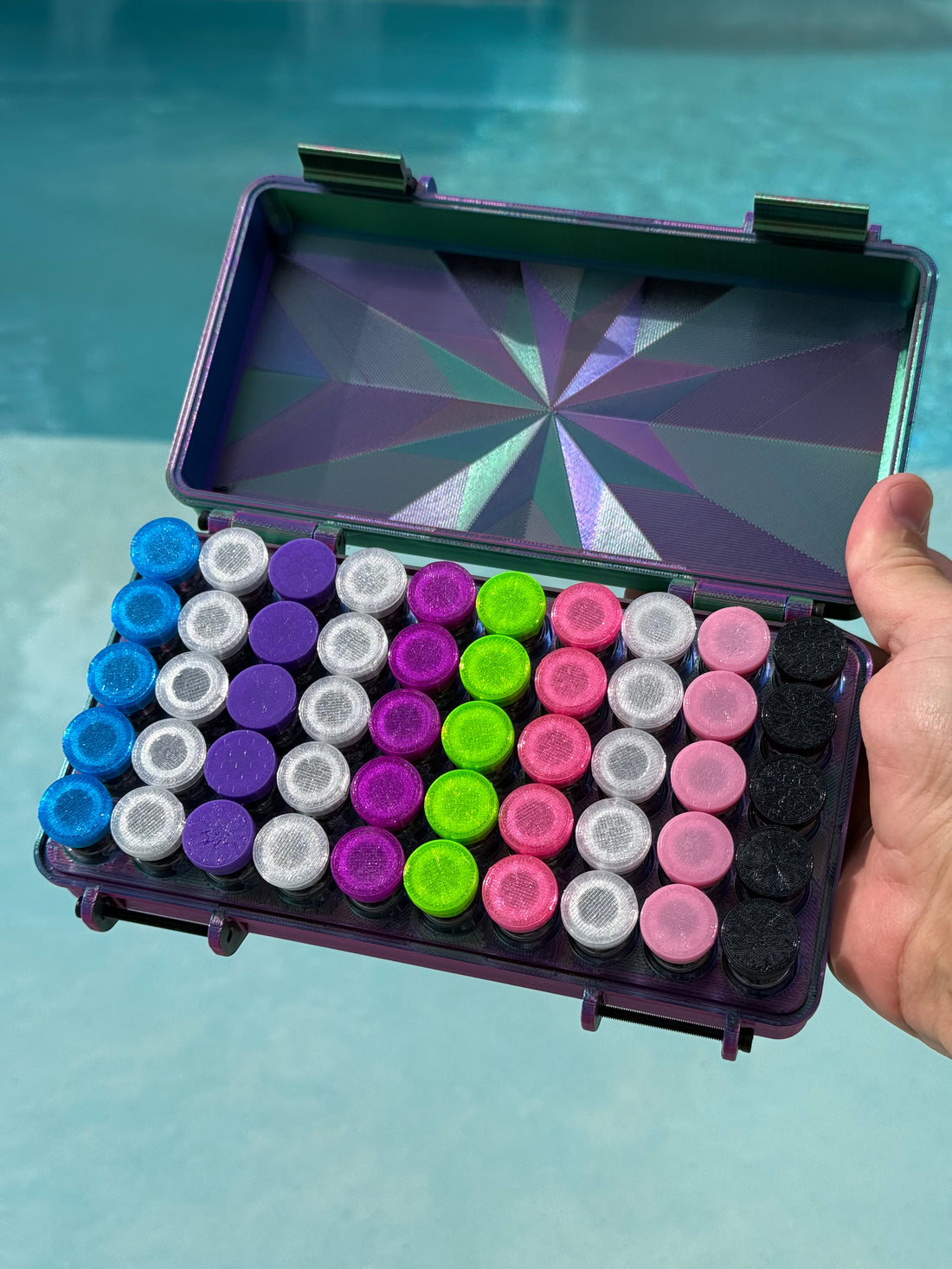 Colorful vial caps in a case held by a hand with a pool background