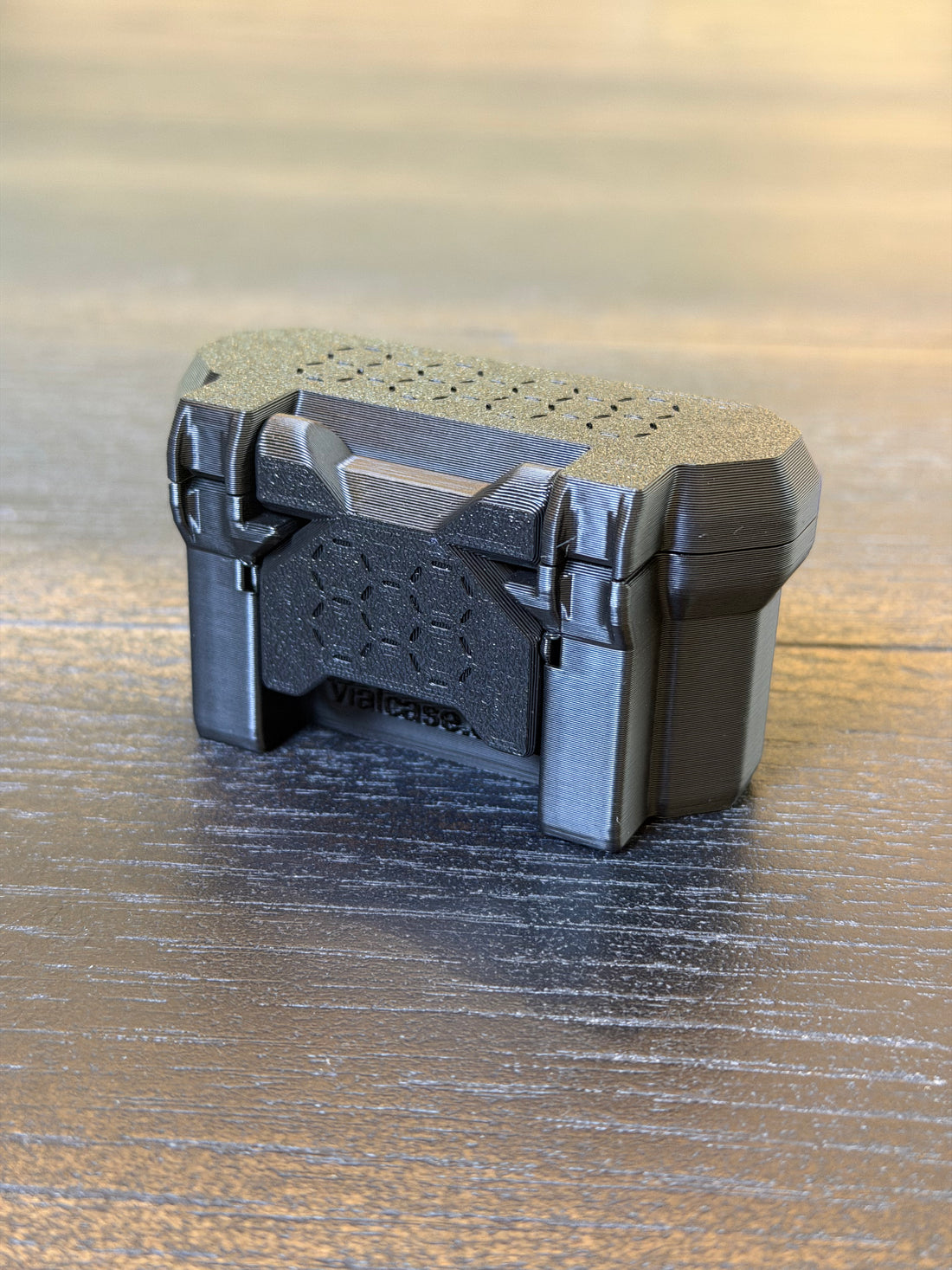 Closed black 3D-printed hard-shell vial case with a textured lid and front latch, shown at a three-quarter angle.